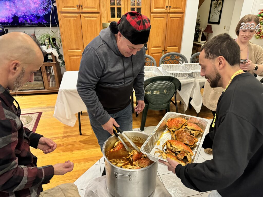 Family members enjoying a New Year's Eve tradition of serving seasoned crab from a large pot during a festive home gathering. Captured by Lorie-Lyn Photography in Freetown, MA